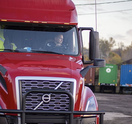 Red truck with a man in the driver seat turning the wheel 