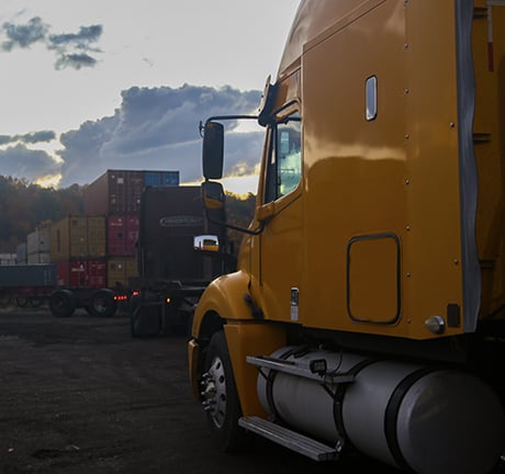 The driver side of a yellow truck in a container yard