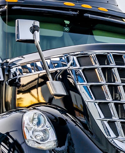 A shiny black shipping truck with a chrome grill and chrome mirror