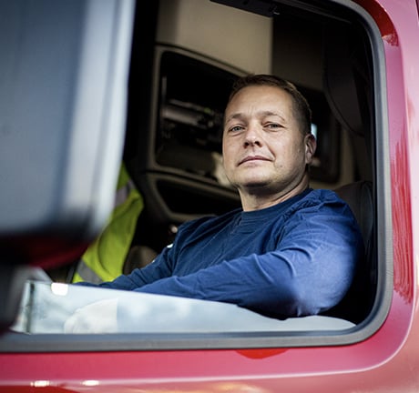 image of a male truck driver sitting behind the driver wheel looking out the window of his driver side diir