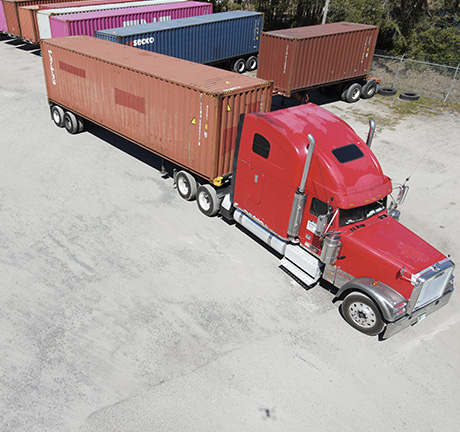 a red shipping truck with a brown container, parked in front of multiple containers.