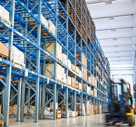 inside of a warehouse, blue holding shelves, a blurred forklift to the right