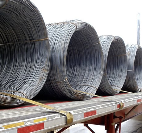 four rolls of bound wire, held down with straps to a flatbed on a shipping truck